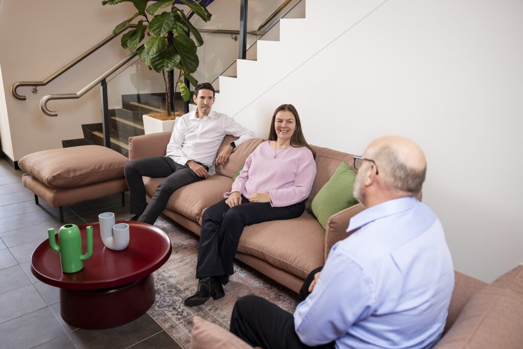 Carers leave: Two people seated on a pink sofa in an office lounge talking with a third man seated opposite in the foreground